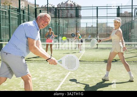 Uomo e donna anziani motivati che giocano a padel con il suo compagno di squadra in tribunale Foto Stock