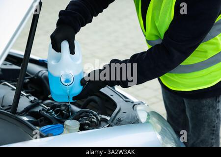 Uomo che versa il lavavetri dal contenitore in plastica nel serbatoio dell'auto all'aperto, primo piano Foto Stock