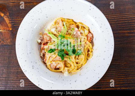 Una generosa porzione di pasta cremosa condita con erbe fresche si trova su un piatto bianco macchiato. Il piatto presenta una ricca salsa ed è presentato elegantemente, Foto Stock