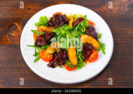 Un'insalata vivace con rucola fresca, pomodori ciliegini e fette di mela abbinate a frutta secca dolce. Il piatto è ben disposto su un tavolo Foto Stock