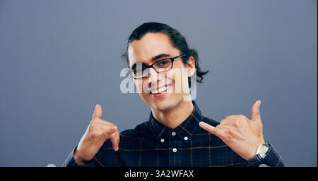 Ritratto, uomo e chiamami firmano in studio, simbolo o emoji di connessione con gli occhiali sullo sfondo. Mani, sorrisi e persona con appendere in libertà, shaka Foto Stock