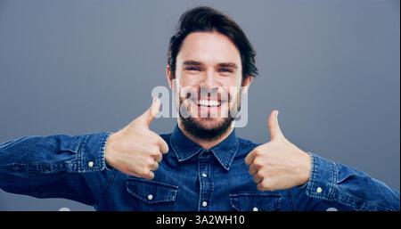 Pollice, sorriso e mani con ritratto dell'uomo in studio per approvazione, successo e feedback. Come emoji, sì firma e accordo con la persona maschile su Foto Stock