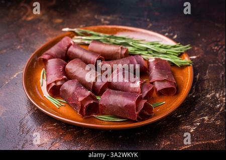 Tipica carne spagnola secca cecina, jamon di manzo spagnolo su piatto con rosmarino. sfondo marrone. vista dall'alto. Foto Stock