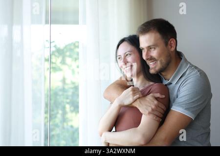 Felice coppia interrazziale che guarda da una finestra a casa Foto Stock