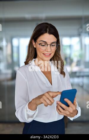 Donna d'affari di mezza età sorridente che usa il cellulare in ufficio. Foto Stock