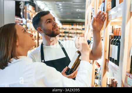 Il proprietario del negozio aiuta una giovane donna a scegliere un buon vino. Foto Stock