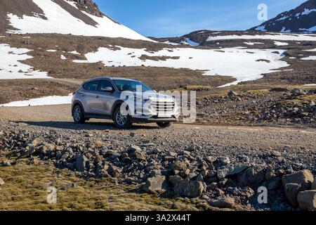 Formazioni rocciose vulcaniche di Arnarfjordur, Westfjords, Islanda, con un fuoristrada 4x4 che guida su tortuose strade sterrate, montagne innevate. Foto Stock