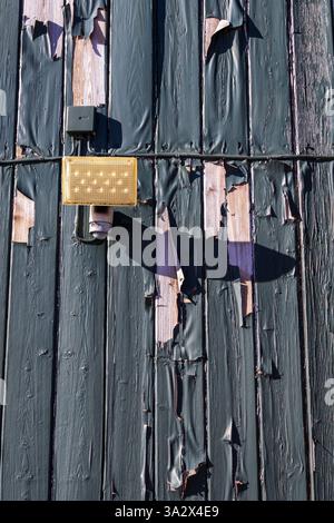 la vernice verde si stacca da una facciata in legno con una tavola, con un cavo elettrico che passa sopra di essa, anch'essa rivestita nello stesso strato resistente agli agenti atmosferici, rivelando l'età Foto Stock