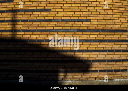 Un muro di mattoni gialli con più linee di mattoni neri viene trasformato da un'ombra, creando un'illusione astratta che assomiglia a una nave stellare ormeggiata Foto Stock