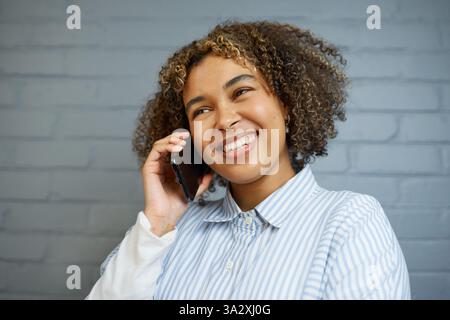 Donna che parla al telefono sorridente in abito casual sullo sfondo di Brick Wall Foto Stock
