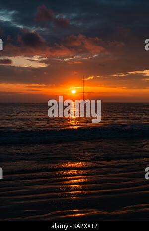 Splendido tramonto sull'oceano con una barca a vela all'orizzonte scattata dalla spiaggia. Foto Stock