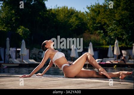 Vista laterale, posizionamento. Donna in bikini bianco è vicino alla piscina. Foto Stock