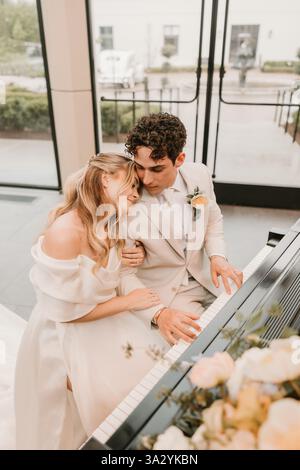 Gli sposi e gli sposi condividono un momento intimo suonando un pianoforte a coda Foto Stock