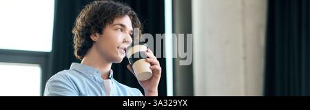 Un bel giovane sorseggia con cura la tazza di caffè mentre ti godi un momento di lavoro. Foto Stock
