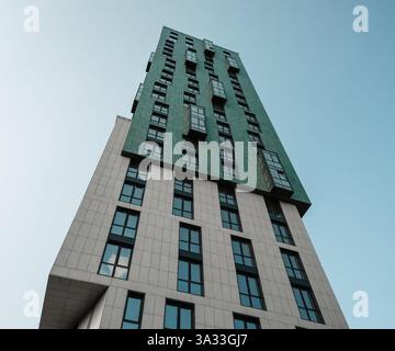 Alta torre residenziale contro il cielo azzurro. Affacciandosi sulla facciata di un edificio moderno con facciata beige e verde. Foto Stock