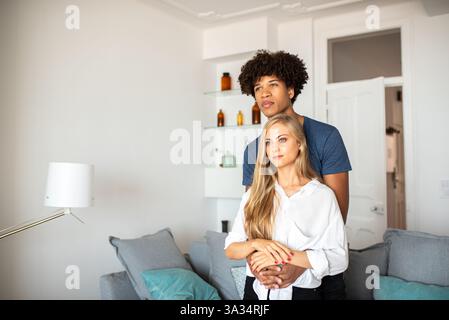 Una coppia condivide un tenero abbraccio nel loro elegante soggiorno. L'illuminazione soffusa e l'arredamento moderno creano un'atmosfera calda e invitante, che mette in risalto il vostro ambiente Foto Stock