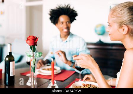 Una cena romantica con due persone che gustano vino e un pasto. Una rosa rossa e una candela creano l'atmosfera, enfatizzando l'intimità e il calore nell'atmosfera Foto Stock