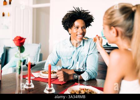 Una coppia gode di una cena romantica a casa, con candele e vino. La scena è intima e calda, con un'attenzione particolare all'esperienza culinaria condivisa An Foto Stock