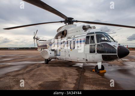 Un elicottero militare bianco con strisce blu e rosse è parcheggiato sull'asfalto bagnato in una base aerea. Le grandi lame del rotore e la struttura robusta sono alte Foto Stock