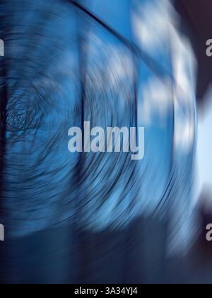 Un'accattivante fotografia astratta caratterizzata da una sfocatura del movimento vorticosa su sfondo blu. L'immagine include sottili riflessi sul vetro, creando Foto Stock