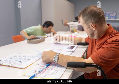 Le persone in un centro diurno per persone con disabilità sono impegnate in attività. Stanno lavorando su progetti creativi, evidenziando un supporto Foto Stock