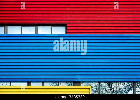 Un'immagine suggestiva che mostra le facciate di un colorato edificio urbano in rosso, blu e giallo vividi, che rappresenta l'uso moderno dei colori architettonici in ci Foto Stock