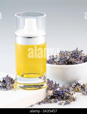 Una bottiglia di vetro riempita con olio di lavanda si trova accanto ai fiori secchi di lavanda. L'essenza rilassante della lavanda evoca relax e calma, perfetto per la vostra vacanza Foto Stock