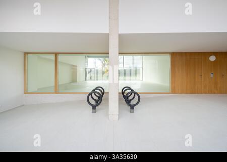 Un interno moderno e spazioso caratterizzato da grandi finestre trasparenti con cornici in legno, due sculture metalliche uniche e una forte colonna verticale. La miscela Foto Stock