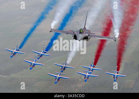 L'aeronautica e spaziale francese Dassault Rafale C, 4-C1, vola in formazione con l'Alpha Jet, mostrando la vernice da esposizione della Patrouille de France. L'aereo emette fumo rosso, bianco e blu come parte di una esibizione aerea, celebrando l'aviazione francese. Foto Stock