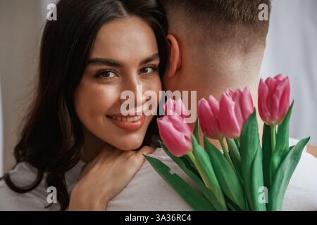 Donna felice con fiori che abbracciano l'uomo. Una giovane coppia è a casa. Foto Stock