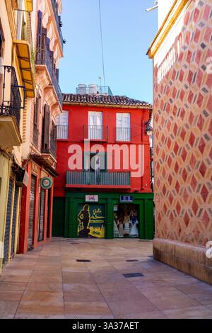 Un vivace edificio rosso con finestre con cornici bianche e balconi in ferro battuto si trova tra edifici storici di Málaga, Spagna. Foto Stock