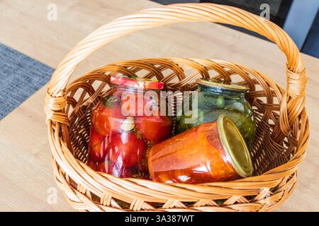 Barattoli con diversi tipi di sottaceti e conserve in un cestino di vimini Foto Stock