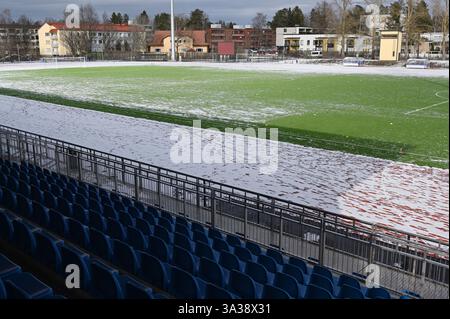 Un campo da calcio parzialmente innevato con erba artificiale, circondato da posti a sedere blu in una struttura sportiva all'aperto. Il freddo e tra Foto Stock