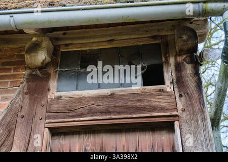 Travi in legno invecchiato e una finestra rotta di un vecchio mulino ad acqua per metà in legno, che mostra trame, crepe e segni di decadimento nella struttura. Foto Stock