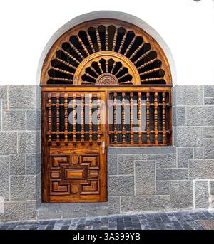 Porta ornata in legno con finestra sullo specchio di poppa con intricate incisioni, incastonata all'interno di una parete in pietra testurizzata, mostra l'artigianato tradizionale e gli archi Foto Stock