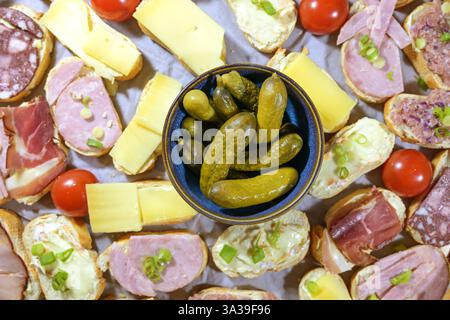 Ciotola di cetriolini circondata da piccoli panini con formaggio, prosciutto e salsiccia, semplice finger food o snack per feste, vista dall'alto, concentrazione selezionata, Foto Stock