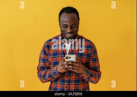 Sorridere e tenere in mano lo smartphone. L'uomo nero e' nello studio su sfondo giallo. Foto Stock