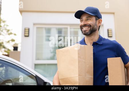 Felice corriere latino di mezza età con indosso l'uniforme blu Foto Stock