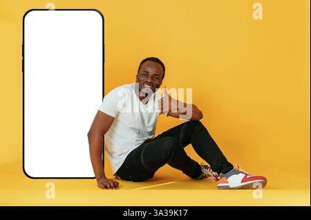 Vicino all'ampio smartphone con spazio per le copie. L'uomo nero e' nello studio su sfondo giallo. Foto Stock