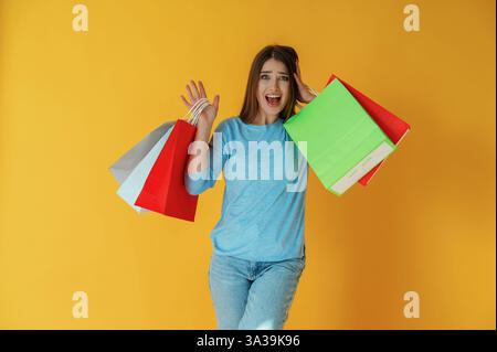 Sorridente, felice, con le borse della spesa. La giovane donna è su sfondo giallo. Foto Stock