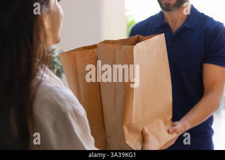 Dipendente maschio addetto alla consegna degli ordini alimentari che consegna pacchi di carta al destinatario Foto Stock