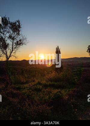 Un'alba vibrante dipinge il cielo con tonalità calde, gettando un bagliore dorato sul paesaggio sottostante. Foto Stock