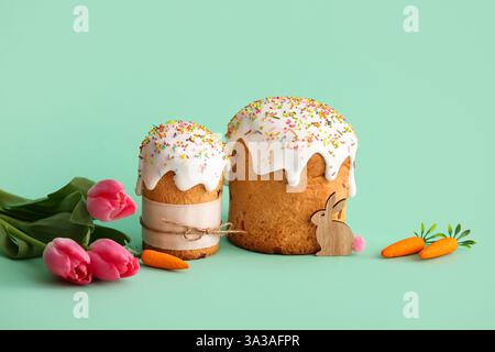 Dolci torte pasquali con mini carote e fiori di tulipani su sfondo turchese Foto Stock