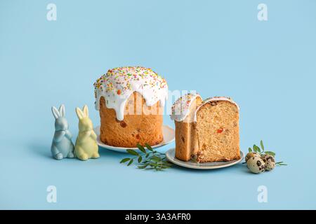 Piatti con dolci torte di Pasqua, uova di quaglia e coniglietti giocattolo su sfondo blu Foto Stock