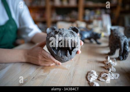 Potter tiene una statuetta di leone dentato a sciabola con mascelle aperte, lavora su una serie personalizzata di gatto in argilla in officina Foto Stock