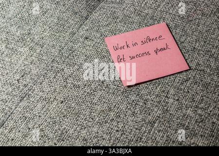 Una nota adesiva rosa con la frase motivazionale Work in Silence lascia parlare il successo su una superficie grigia testurizzata. Questo display enfatizza gli inspirati Foto Stock