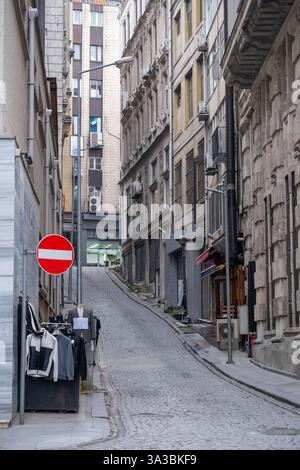 Stretta e storica strada acciottolata senza cartello d'ingresso nel quartiere urbano, caratterizzata da edifici antichi, bancarelle del mercato di strada e dal fascino della città d'epoca. Foto Stock