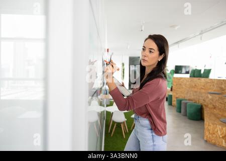 Giovane donna seria che scrive su una lavagna Foto Stock