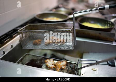 Chef professionista friggere la pakora in un cestello immerso in olio bollente all'interno di una vivace cucina, utilizzando un wok e una padella per preparare piatti autentici Foto Stock