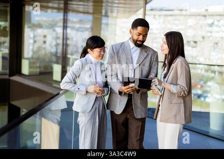 Tre colleghi si riuniscono in un ufficio luminoso, partecipando a una discussione mentre esaminano un tablet insieme. L'atmosfera è piena di creatività Foto Stock